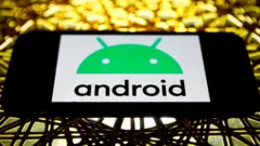 The Android logo on a phone screen in landscape mode, placed on an elaborate metal table lit in golden light
