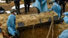 Emergency workers take a coffin out of a grave