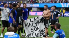 Vários jogadores de futebol argentinos em um campo, segurando uma faixa com os dizeres "Las Malvinas Son Argentinas".