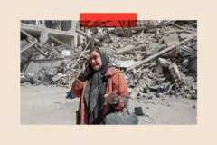 Una mujer con chaqueta naranja y pañuelo gris en la cabeza habla por teléfono frente a un edificio destruido.
