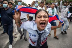 Uma manifestante segurando uma bandeira do Nepal e gritando algo durante um protesto. É possível ver vários manifestantes atrás dela
