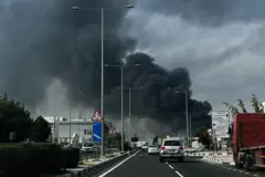 Uma espessa fumaça cinza-escura sobe ao fundo de uma rodovia após um ataque iraniano relatado no distrito industrial de Doha