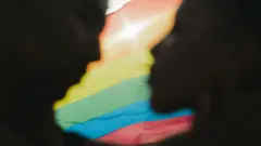 A silhouette of two people in front of a rainbow flag