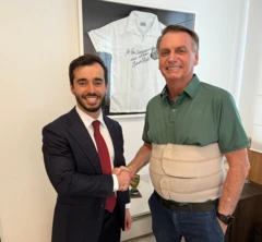 Foto de Ricardo Pita, usando terno azul marinho e gravata vermelha e Jair Bolsonaro, usando cinta de compressão creme e camisa polo verde