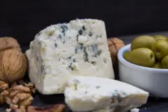 Un pedazo de queso azul como parte de una tabla con nueces de macadamia y aceitunas verdes