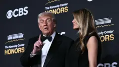Дональд Трамп и Мелания Трамп на фоне стены с надписью Кеннеди-центр, Трамп в смокинге с бабочкой