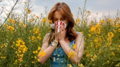 sarı renkli kır çiçekleri arasında elinde mendil ve gözleri kapalı halde hapşıran bir kadın