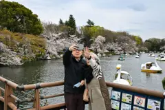 Una pareja de ancianos se toma un selfie con su móvil frente a un estanque lleno de barcos con flores de cerezo en el parque Inokashira en Tokio, Japón.