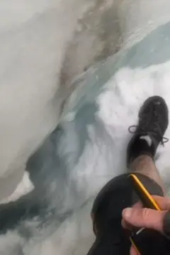 A foto do interior da fenda mostra um buraco mais profundo sob os pés de Jan. O shorts, o tênis de Jan e sua mão segurando o walkie-talkie também aparecem na imagem