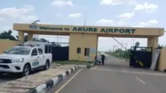 Ẹnu ọna abawọle Papakọ ofurufu Akure.
Ọkọ agbofinro duro siwaju ibẹ, ti awọn asọna si si ẹnu ọna kan silẹ ninu meji