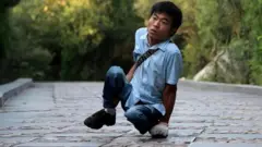 Li Chuangye usa a mão como apoio extra enquanto caminha, em posição agachada.