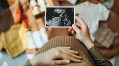 Barriga de uma mulher grávida e uma mão segurando um ultrassom