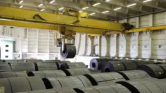 Foto de bobinas de aço sendo carregadas para exportação.