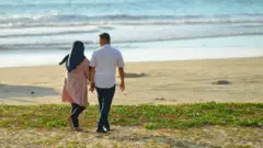 Seorang pria dan perempuan bergandengan tangan di Pantai Lhoknga, Aceh.