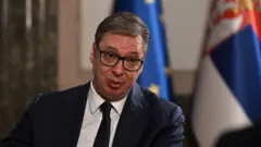 Александр Вучич дает интервью на фоне флага ЕС и флага Сербии.