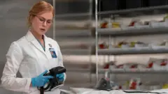 Кадр із серіалу "Скарпетта" - жінка в білому халаті з фотоапаратом