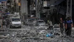 በፍንዳታ የተጎዳ ሕንጻ እና መኪኖች የሚታዩበት በፍርስራሽ የተሸፈነው የጋዛ ከተማ ሪማል አካባቢ መንገድ