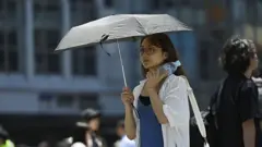 2025年6月17日に東京で、日傘を差し、水のペットボトルを首にあてながら歩く女性