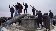 مجموعة من المدنيين يحطمون تمثالاً لمقاتل من قوات سوريا الديمقراطية في مدينة الطبقة بعد سيطرة الجيش السوري عليها، في الطبقة، سوريا.
