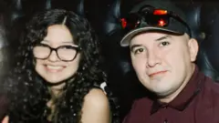 Ofelia Torres suena a la cámara mientras se encuentra sentada al lado de Rubén Torres.