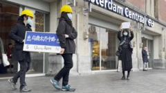 夏巢川在阿姆斯特丹舉起一張白張，有兩人裝扮成建築工人搬走寫上「烏魯木齊中路」的路牌裝置