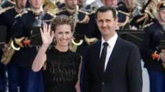 Ex-presidente sírio Bashar al-Assad (à direita) egloboesporte fluminenseesposa Asma (à esquerda) durante um jantar na cúpula UE-Mediterrâneogloboesporte fluminenseParisgloboesporte fluminense13globoesporte fluminensejulhogloboesporte fluminense2008. Asma acena para o público. Atrás deles estão membros da Banda Presidencial da França.