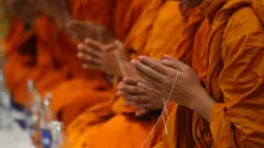 Primer plano de las manos de una fila de monjes, juntos en oración.