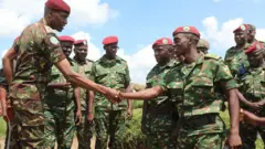 Umugaba mushya w'izi ngabo z'akarere Major General Aphaxard Muthuri Kiugu  (ibumoso) mu kwezi gushize yatangiye imirimo mishya, hano araramutsa umusirikare w'Umurundi aho bakorera muri Masisi