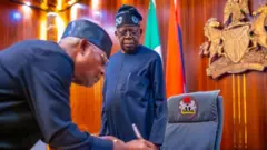 Vice Admiral Ibok-Ete Ibas (Rtd) signin on paper while President Bola Tinubu watches