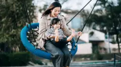 Mulher em um parquinho, sentada com criança em um balanço