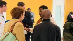 Abagore n'abagabo bo ku ruhande rwagiriza Charles Onana barimo baganira mu kirongozi c'inzu bakoze uruziga, umugore umwe akoze ikimenyetso n'ikiganza