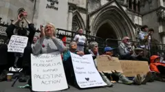 Несколько сторонников Palestine Action в понедельник утром у здания Королевского суда. На снимке видно шесть плакатов в поддержку организации, которые люди держат в руках 