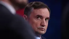 Mężczyzna w garniturze i krawacie spogląda w prawo z zaniepokojonym wyrazem twarzy.