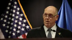 Том Хоман, пожилой лысый мужчина, на фоне американского флага.