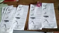 টেবিলের ওপর কয়েকটি ব্যালট পেপার রাখা। সেগুলোয় লাঙল, নৌকা, ধানের শীষ, কাচি ও হাতপাখা প্রতীক রয়েছে