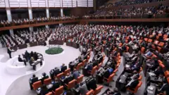 Meclis'te genel kurulun yandan görünümünde milletvekilleri koltuklarında, ortadaki kürsüde bir vekil konuşuyor, başkan ve vekilleri de ortadaki dairesel masada. 