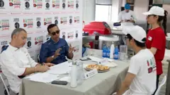 Pessoas sentadas em uma mesa conversando. Há uma pizza na mesa