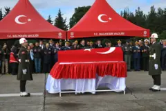 İbrahim Polat'ın cenaze töreninden bir fotoğraf. Üzerinde Türk bayrağı örtülü bir tabutun başında üniformalı iki asker bulunuyor. Arkada yetkililer ve yakınlar ellerini açarak dua ediyor. 