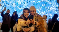 božić, proslava božića, dve devojke se slikaju ispred novogodišnjih ukrasa