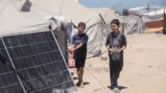 Dois meninos próximos de um painel solar e várias barracas