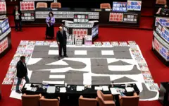 2025年3月28日，執政民進黨立委柯建銘站在立法院一張寫有「罷免」字樣的海報上