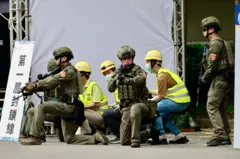Militares com armas protegendo pessoas que estão abaixadas na rua