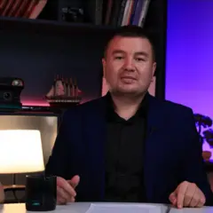 Qora kostyum kiygan, yumshoq yuzli, kalta sochli erkak ekranga qarab turgan rasmi