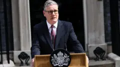 Keir Starmer egy pódium mögött áll, sötétkék öltönyben és lila nyakkendővel.
