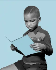 Imagem em preto e branco com fundo azul claro. Um menino está sentado e segura uma folha de papel azul nas mãos, olhando para ela com expressão séria. Uma lágrima escorre pelo seu rosto. Ele veste camisa de manga longa com detalhe listrado no peito e shorts