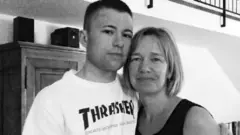Dylan e Seonaid Stallan abraçados dentro de casa, em foto em preto e branco