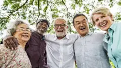 five elderly people hug and smile