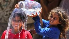 A Palestinian girl pours water over another girl, who is smiling 