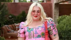 Felicity Hayward con gafas de sol rosadas y vestido rosado