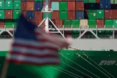 Bandeira americana tremula em frente a navio com contêineres